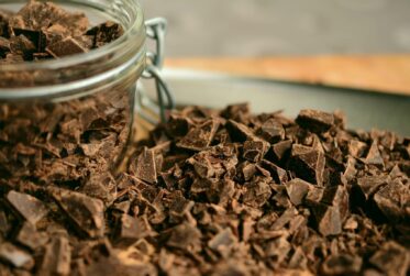 A jar of chocolate chips on top of some chopped up chocolate.