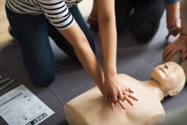 CPR training session showing chest compressions on mannequin with first aid booklet