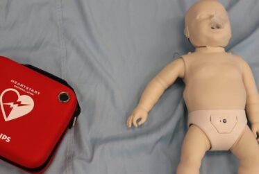 A baby doll and a red case on the bed.